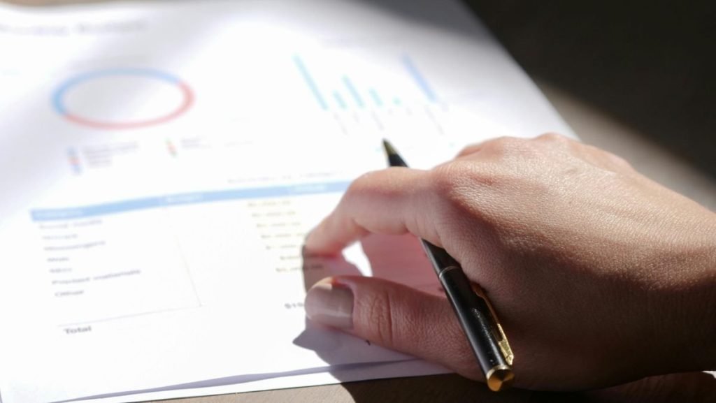 Mão segurando uma caneta e analisando gráficos financeiros, representando a educação financeira para iniciantes.