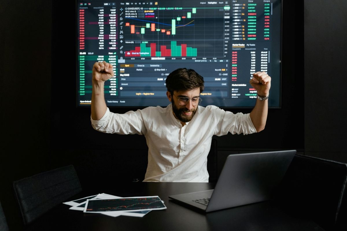 Homem celebrando o sucesso nos primeiros investimentos após estudar gráficos financeiros, simbolizando o resultado da autonomia e do dinheiro trabalhando por você.