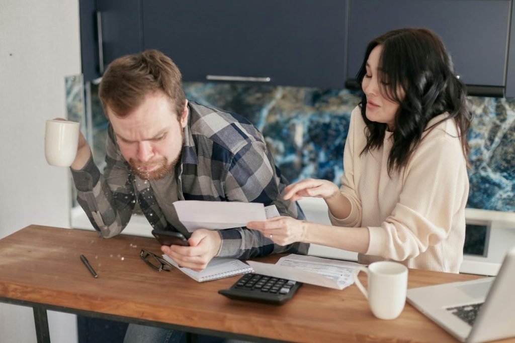 Juros e Dívidas: Casal estressado olhando contas e calculadoras para entender o endividamento.