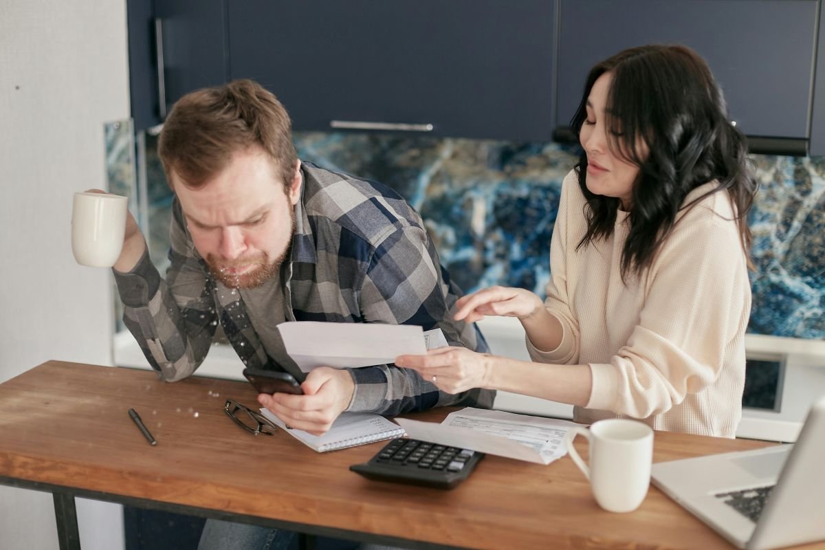 Juros e Dívidas: Casal estressado olhando contas e calculadoras para entender o endividamento.
